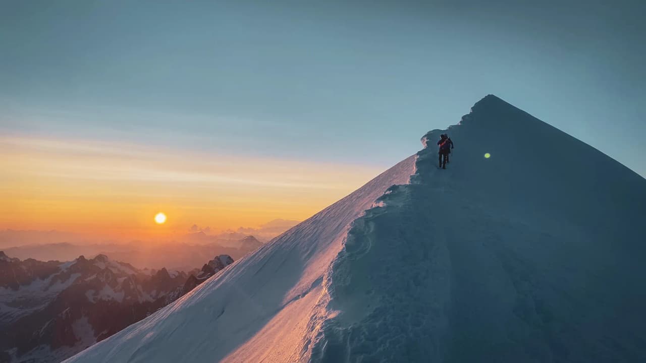 Een klimmer bedwingt de besneeuwde top van de Mont Blanc onder een spectaculaire zonsondergang.