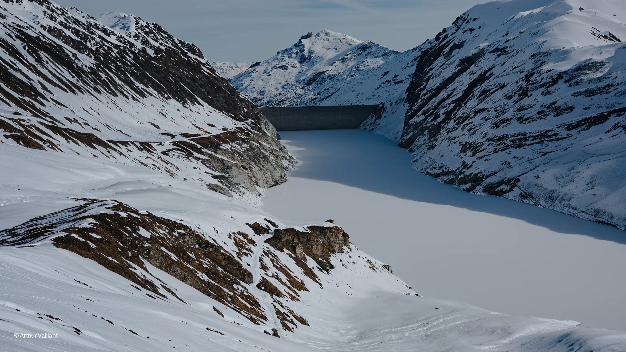 A spectacular Alpine panorama featuring snow-capped mountains and a frozen lake, inviting you to set off on an adventure.