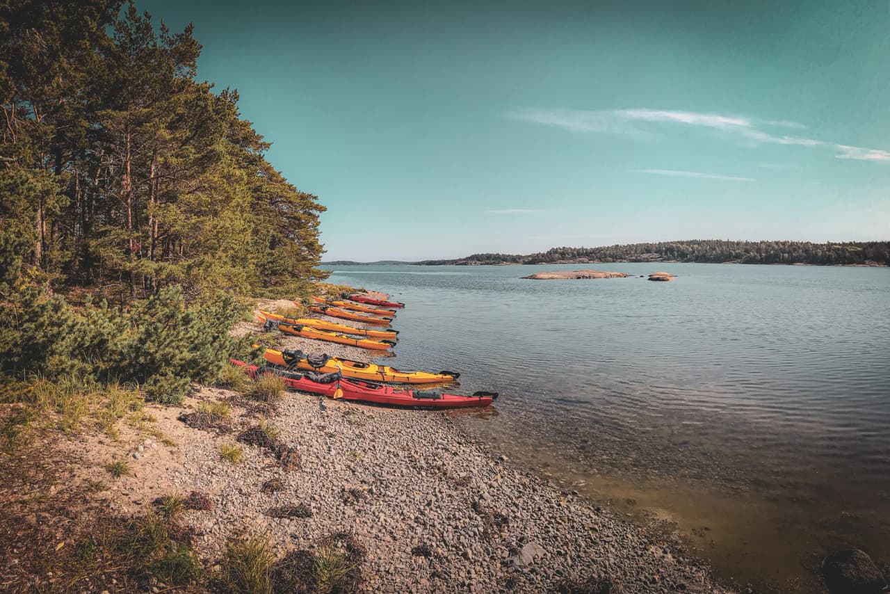 Colourful kayaks moored on a pebble beach, surrounded by Nordic countryside, are an invitation to adventure.