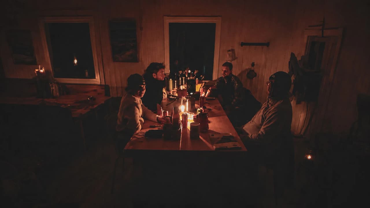 Groupe de voyageurs autour d'une table éclairée à la chandelle, ambiance chaleureuse en Laponie.