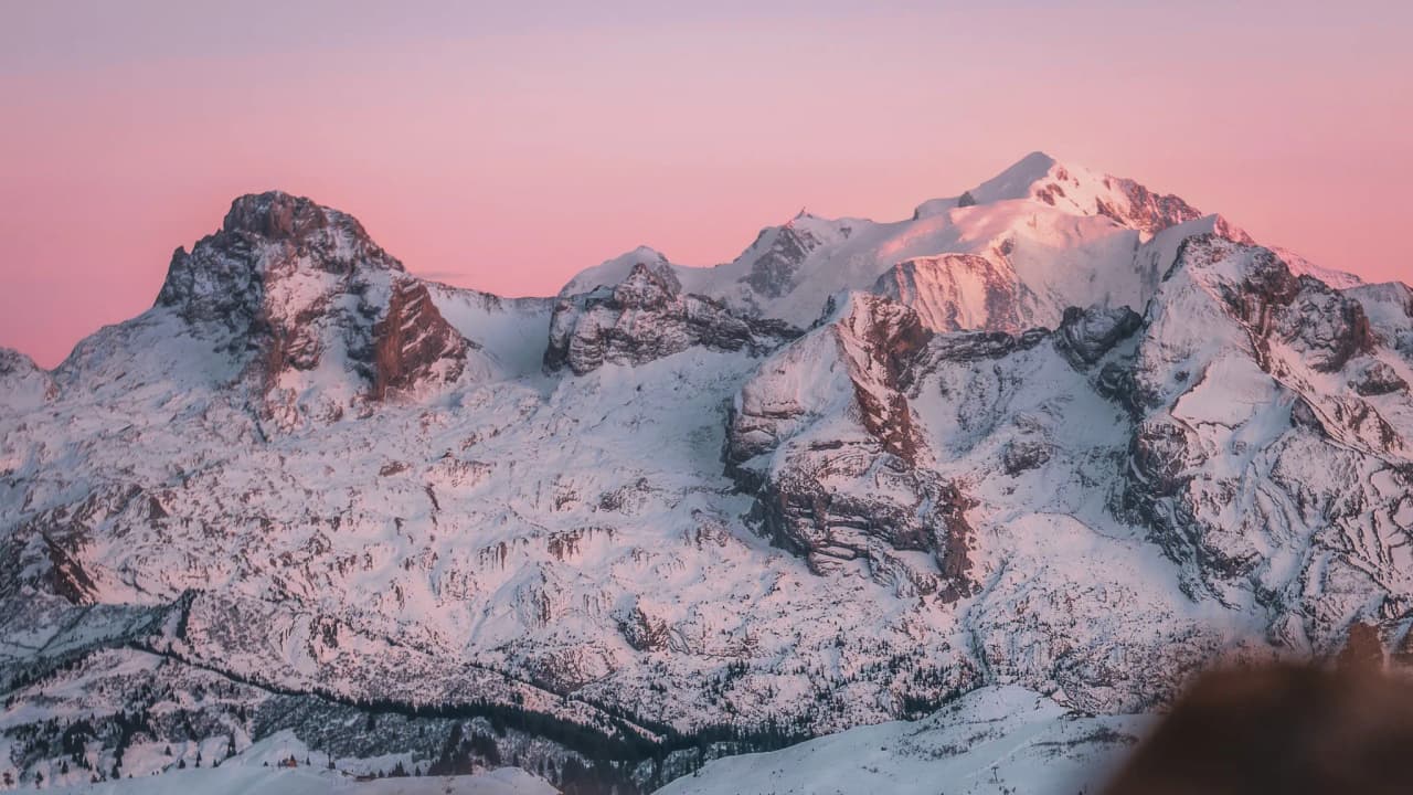 A magnificent alpine landscape at dusk, with snow-capped peaks bathed in shades of pink and orange.