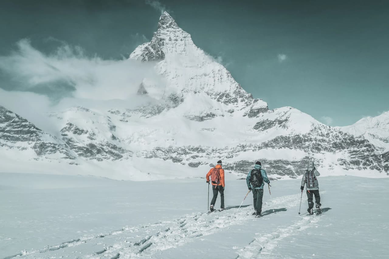 Trois skieurs explorent un glacier sous un majestueux sommet enneigé, ambiance alpine sauvage.