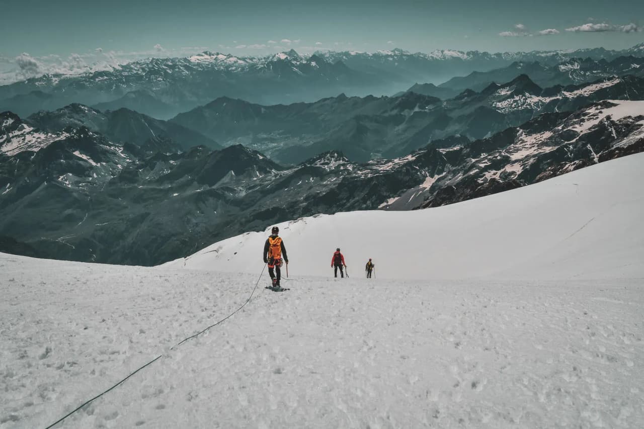 Alpinistes progressant sur un glacier blanc, avec les majestueuses montagnes en arrière-plan.
