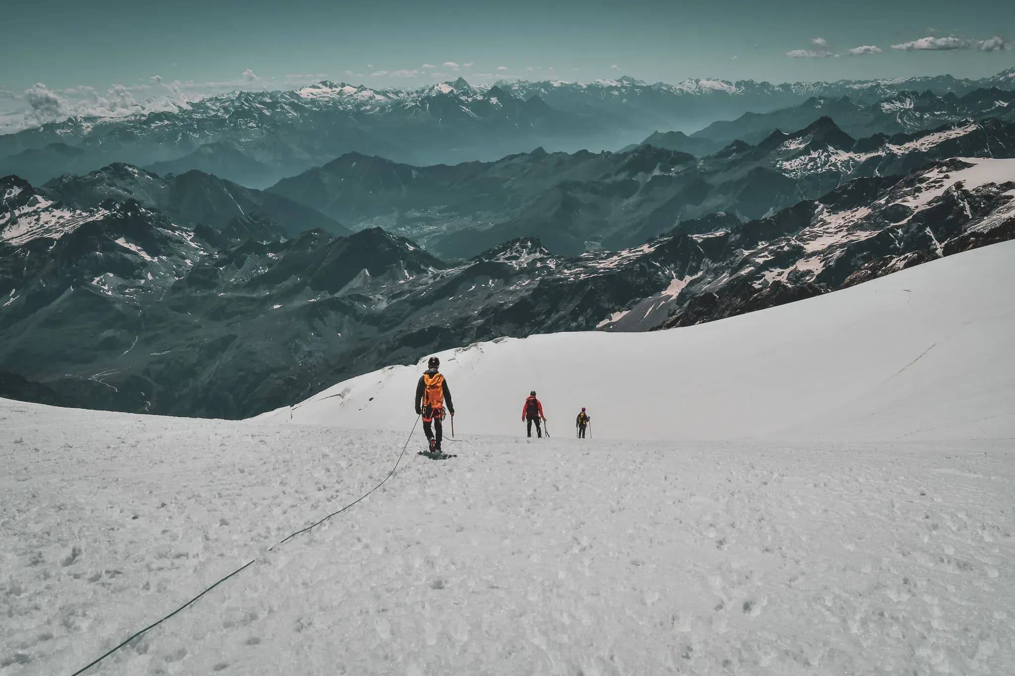 Alpinistes progressant sur un glacier blanc, avec les majestueuses montagnes en arrière-plan.