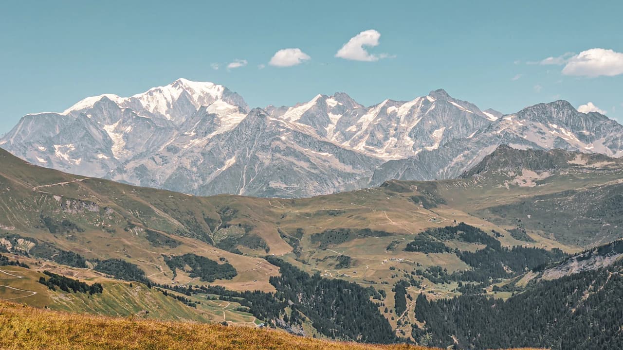 Majestueux paysage alpin avec des sommets enneigés, vallées verdoyantes et ciel bleu, invitation à l'aventure.