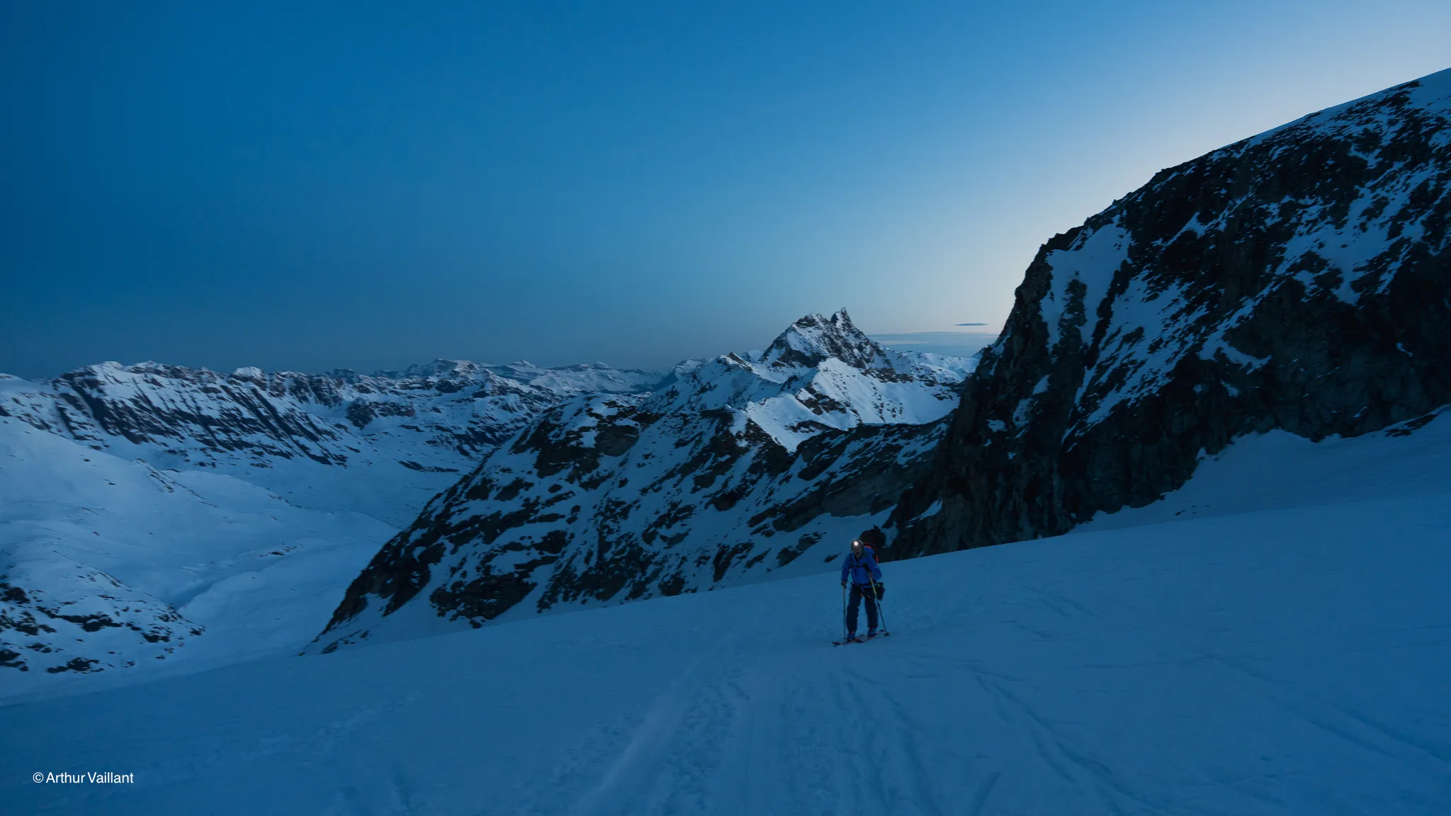 A lone skier at the first light of day, on the snow-covered slopes of the majestic Alps.