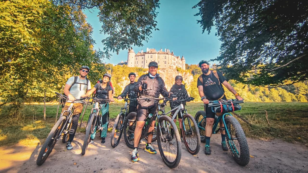 A group of smiling adventurers with mountain bikes in front of a castle, in the heart of the wilderness.