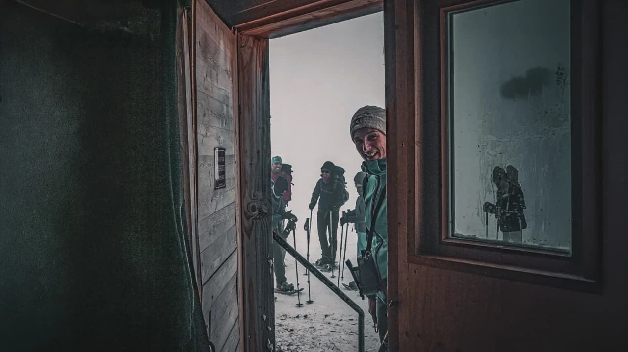 Groupe d'aventurières souriantes devant une cabane en pleine montagne, prêtes pour l'expédition.