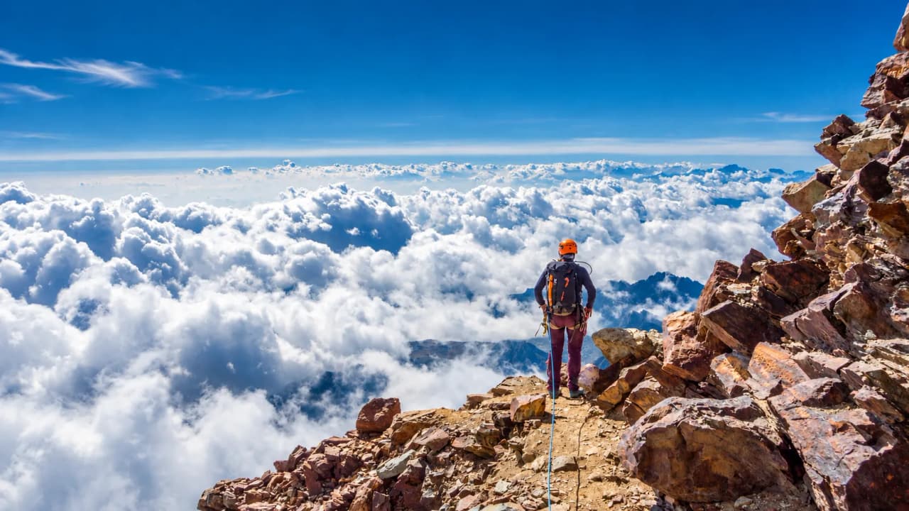 A mountaineer takes in a breathtaking view above the clouds from the summit of a mountain.