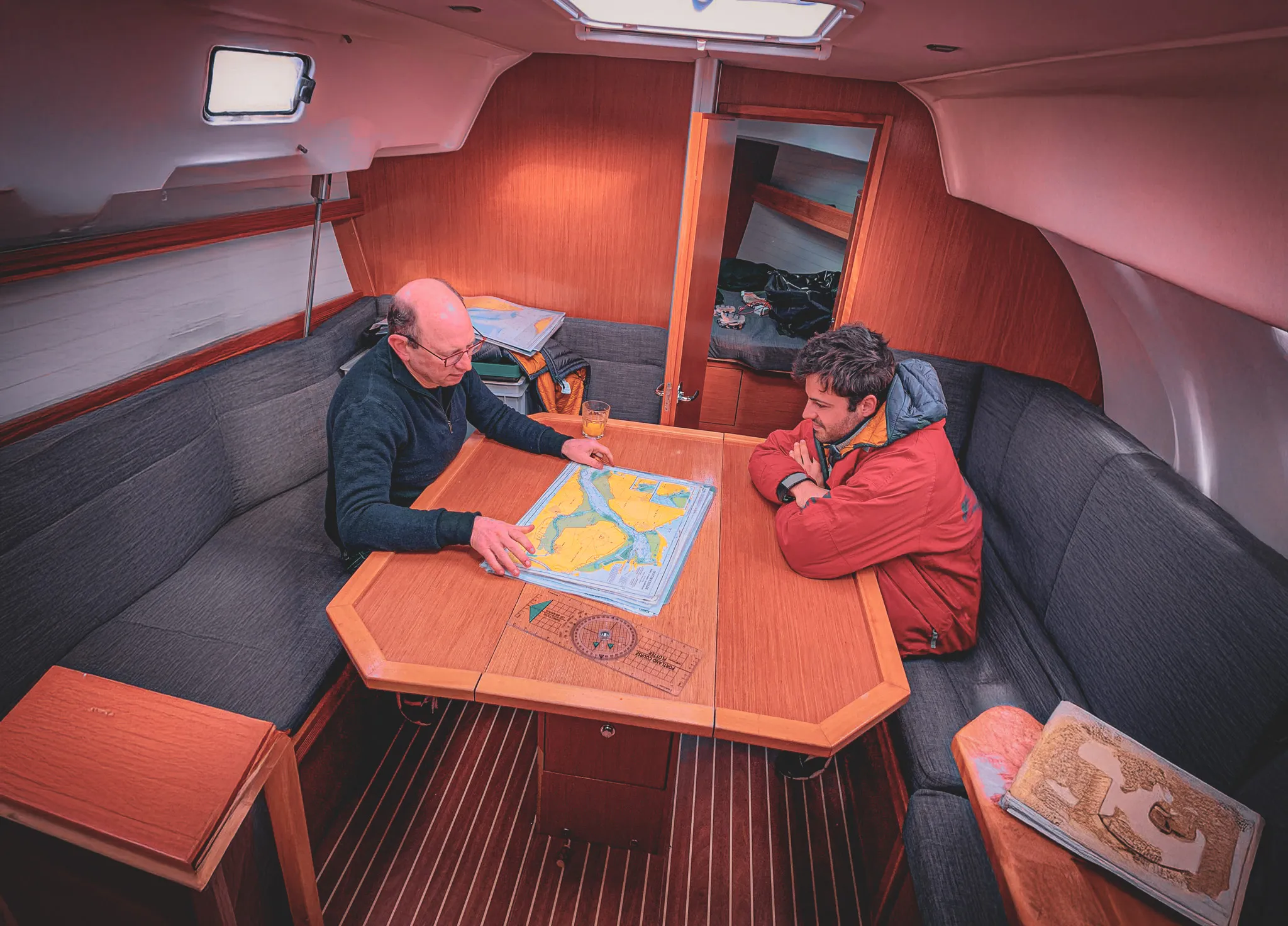 Deux hommes étudient une carte nautique dans un voilier, prêts pour une aventure en Zélande.