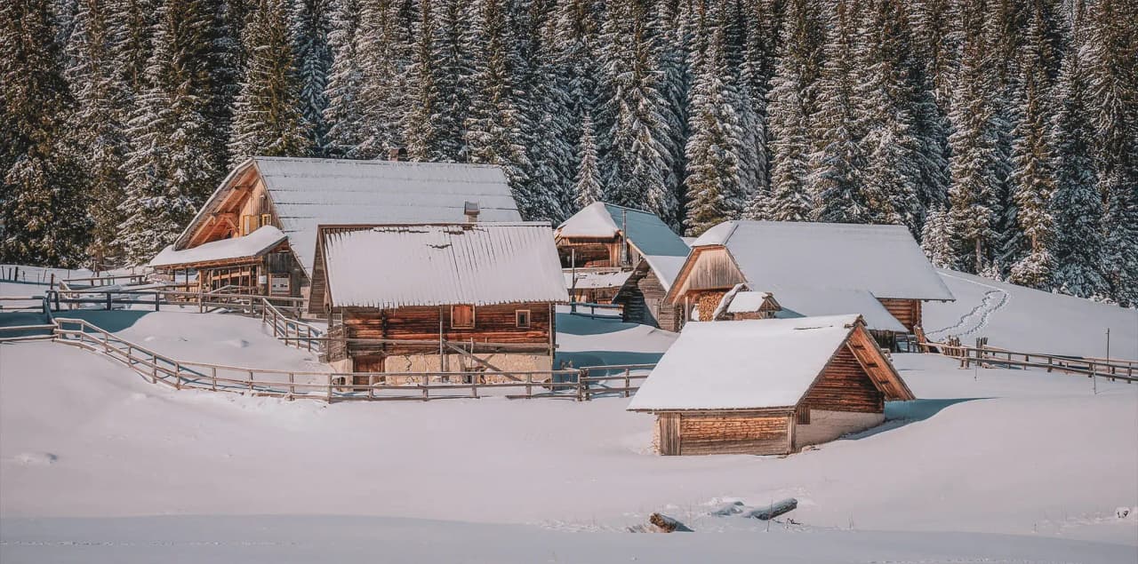 Charmantes cabanes enneigées entourées de forêts majestueuses dans les Alpes juliennes.