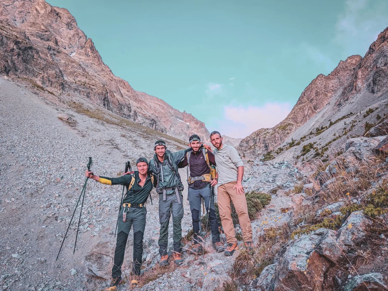 Four smiling mountaineers pose on a mountain path in the Ecrins, ready to conquer the summits.