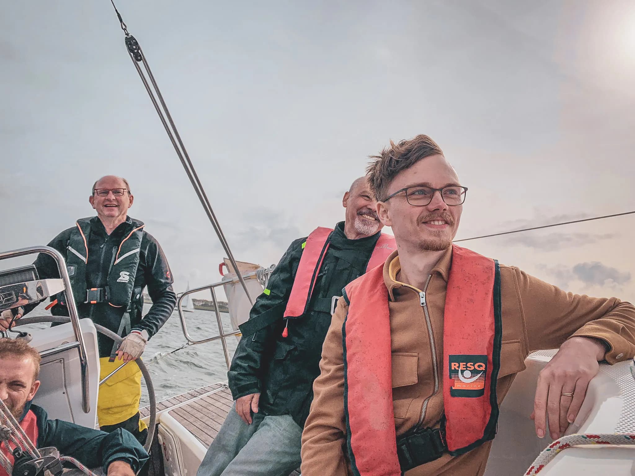 Groupe souriant en mer, apprenant la voile, ambiance conviviale et aventure en Zélande.