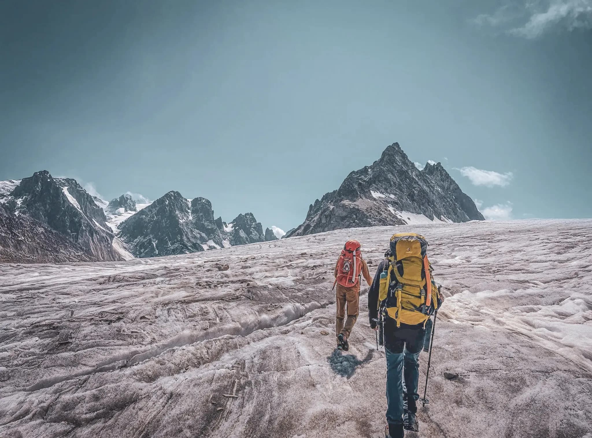 Two climbers on a glacier, surrounded by the majestic peaks of the Ecrins under a blue sky.