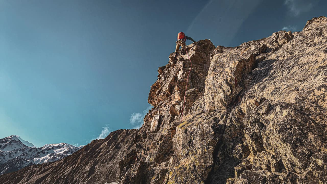 Alpiniste escaladant une paroi rocheuse dans les Écrins sous un ciel bleu éclatant.