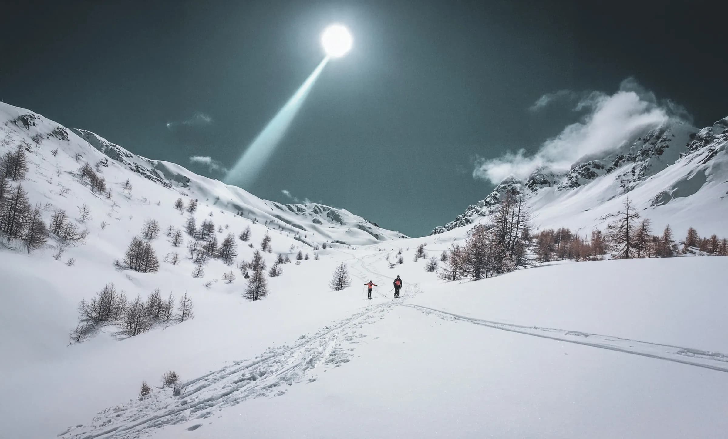 Deux skieurs explorent un paysage alpin enchanteur, sous un ciel lumineux et enneigé.