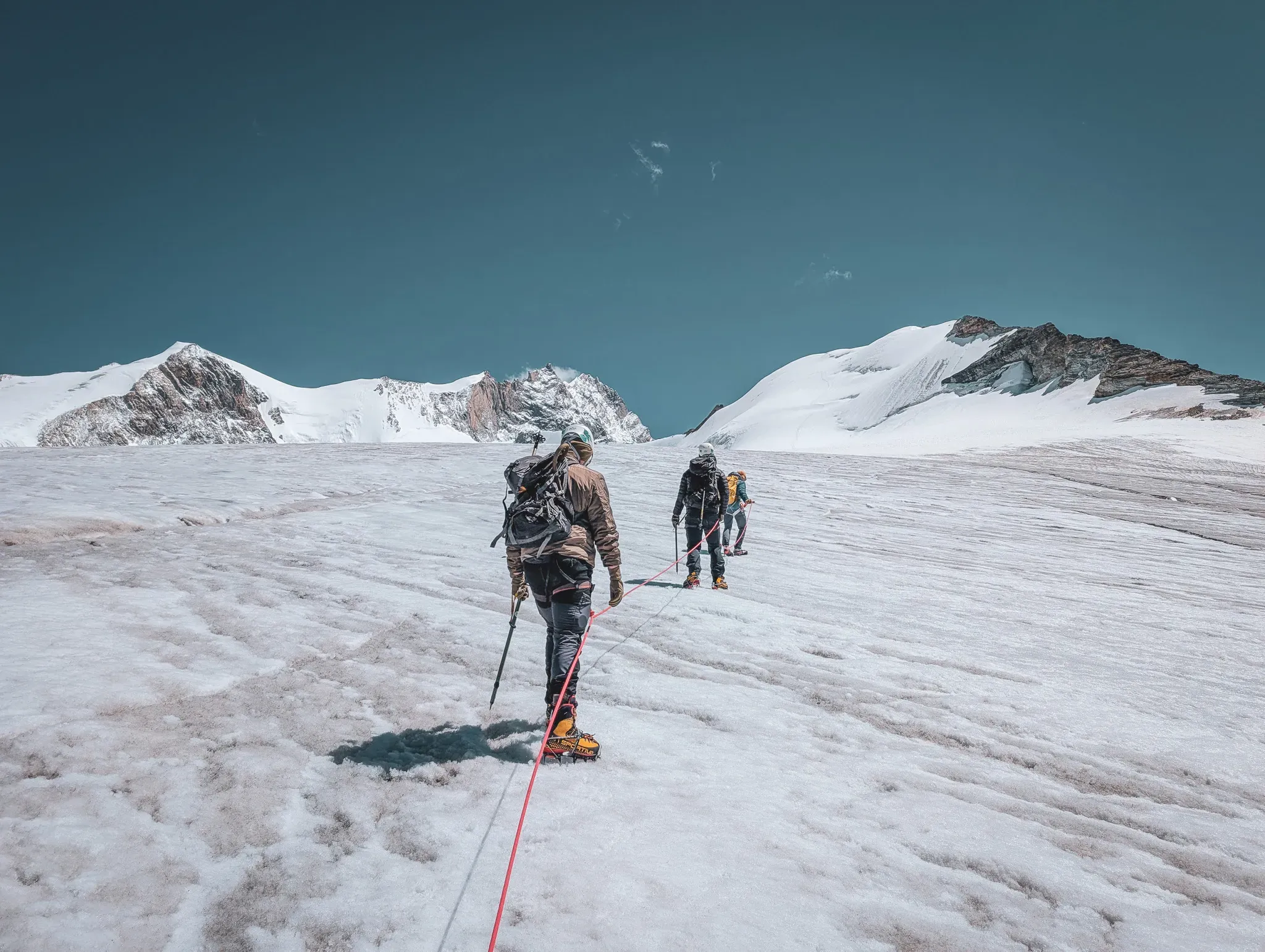 Mountaineers on a glacier, heading towards the majestic Bishorn, under a blue sky.