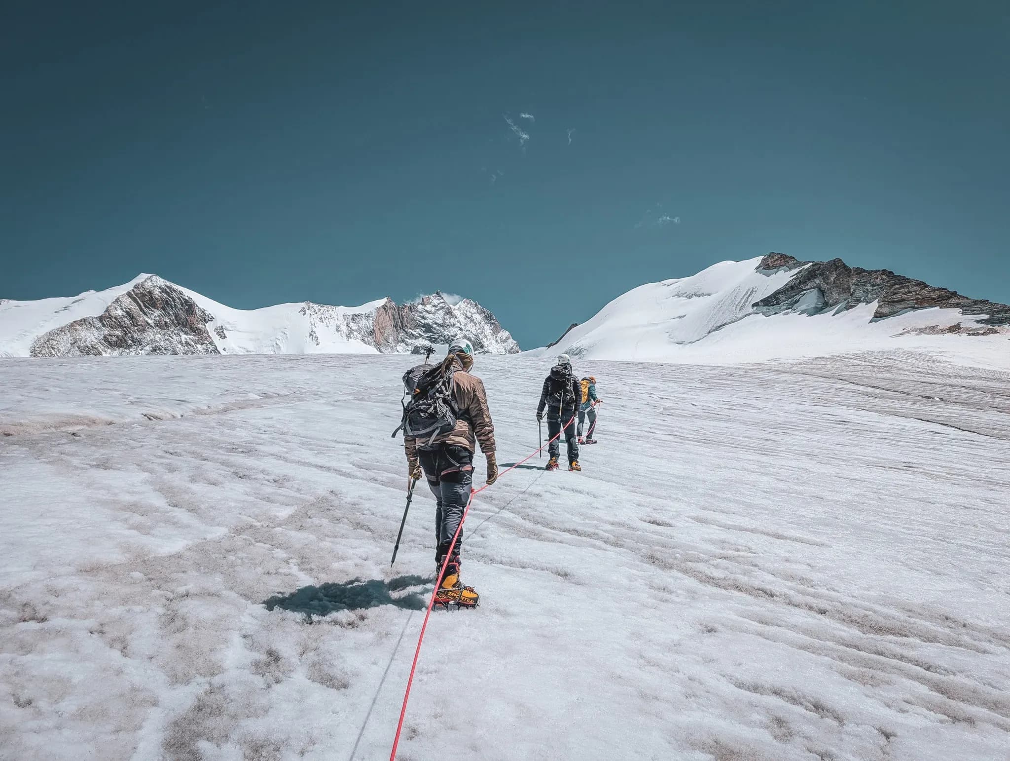 Mountaineers on a glacier, heading towards the majestic Bishorn, under a blue sky.