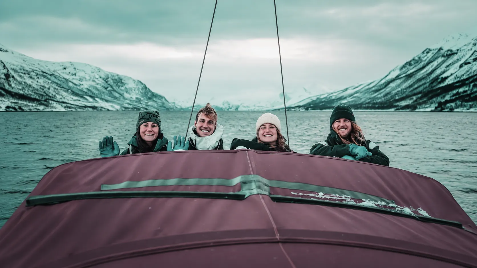 Four smiling friends on a boat, surrounded by the spectacular snowy scenery of the Lyngen Alps.