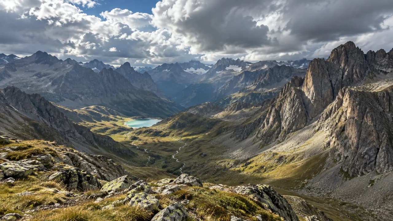Vaste panorama des Alpes, vallées verdoyantes et lacs explosant de couleurs sous un ciel nuageux.