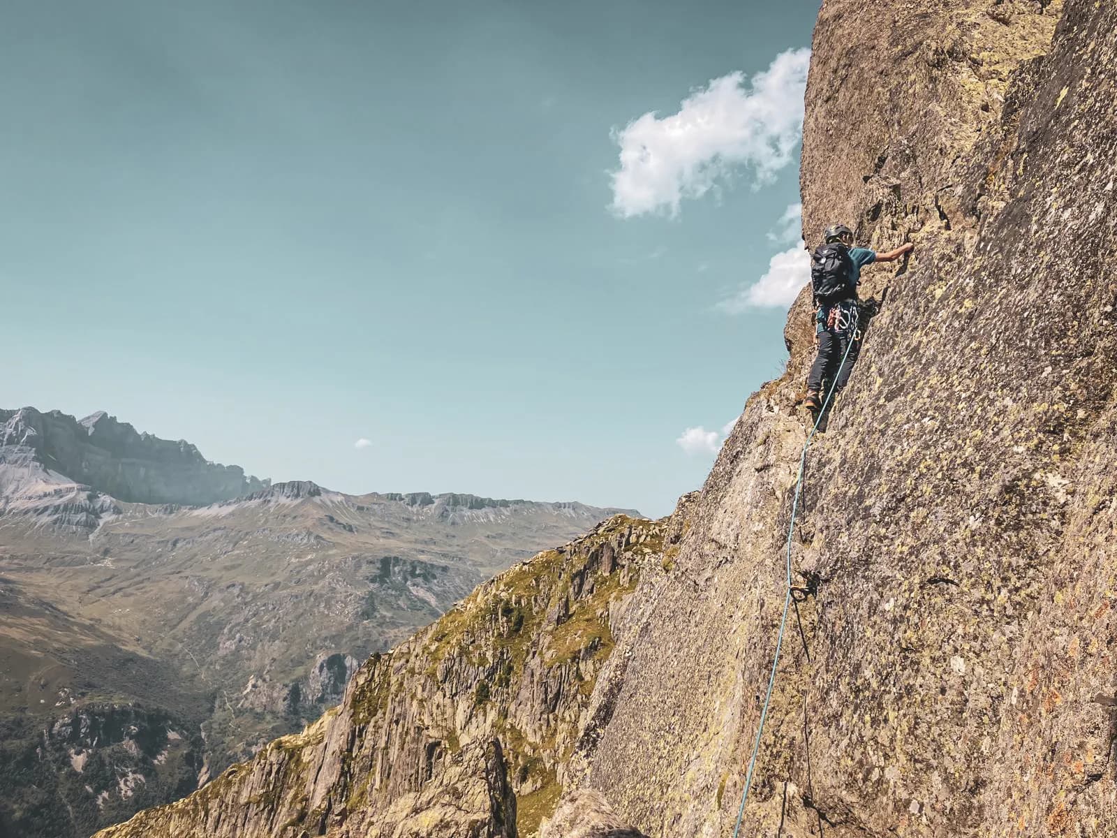 A mountaineer climbs a rock face with a breathtaking mountain panorama.