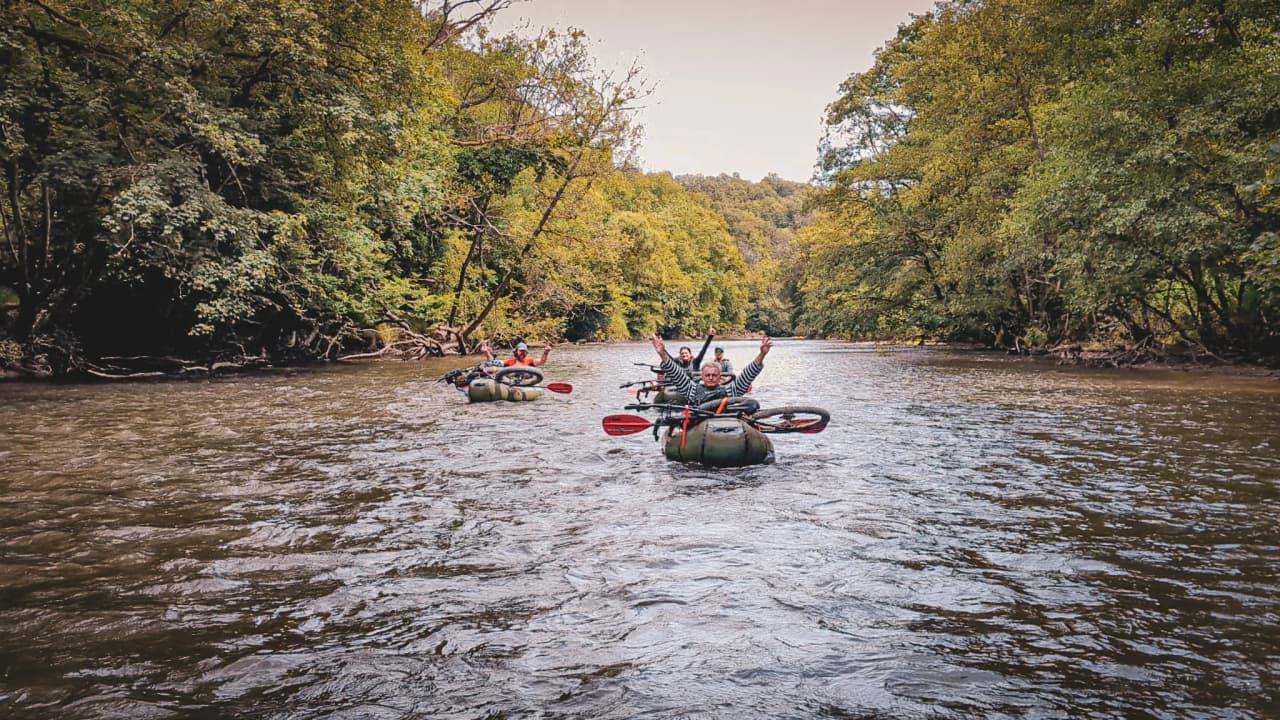 A group of packraft adventurers on the River Lesse, surrounded by lush green countryside.