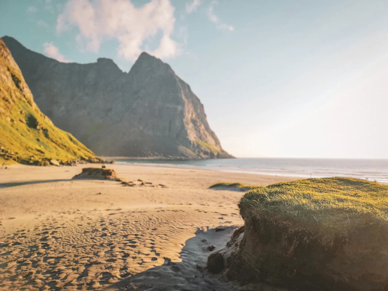 A majestic beach in Lofoten, with green mountains and sun glinting off the sand.