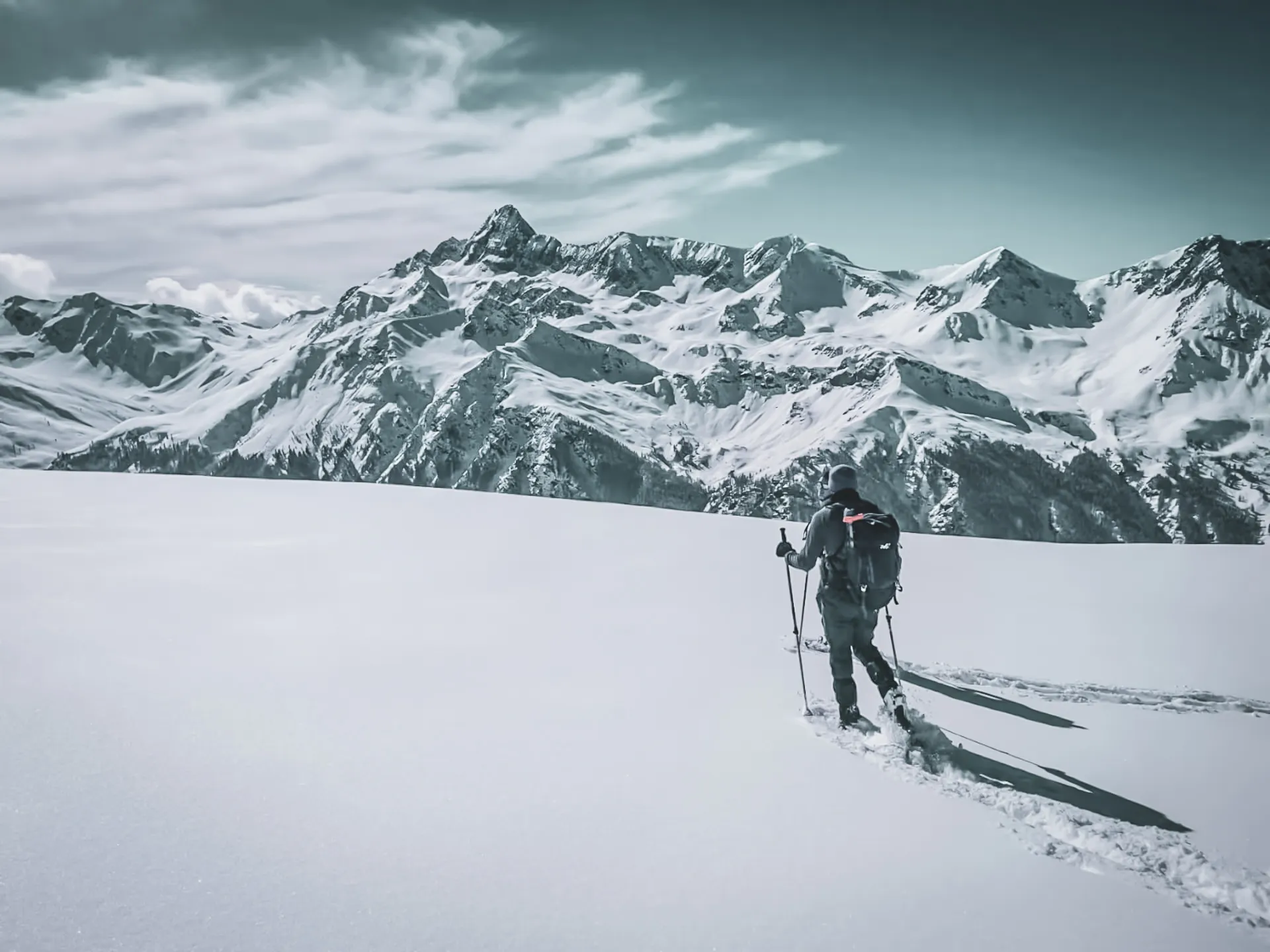 A hiker on snowshoes makes his way through a snow-covered mountain landscape, inviting you to get away from it all.