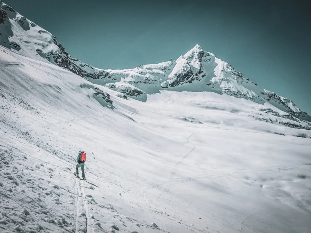 Un skieur solitaire s'attaque aux pentes enneigées du Grand Paradis, sous un ciel bleu éclatant.