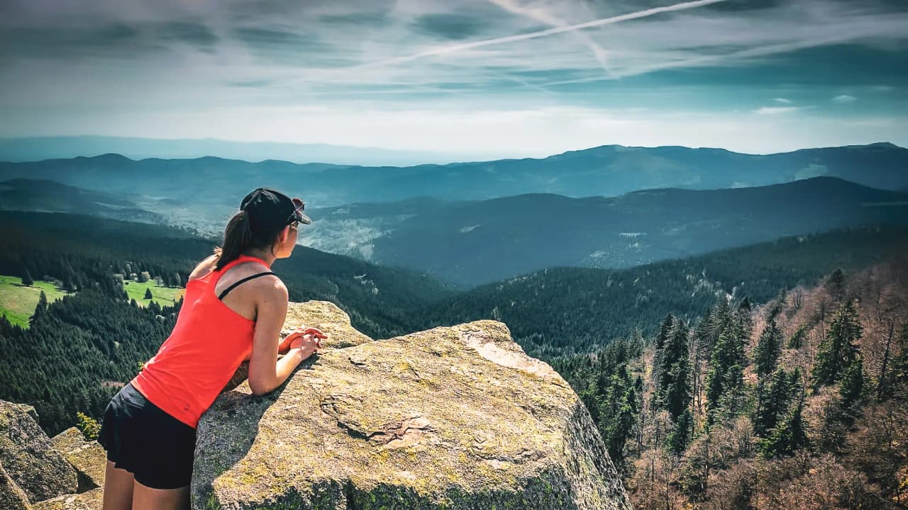 Hiker admiring a mountain panorama from a summit in the Vosges, clear sky.