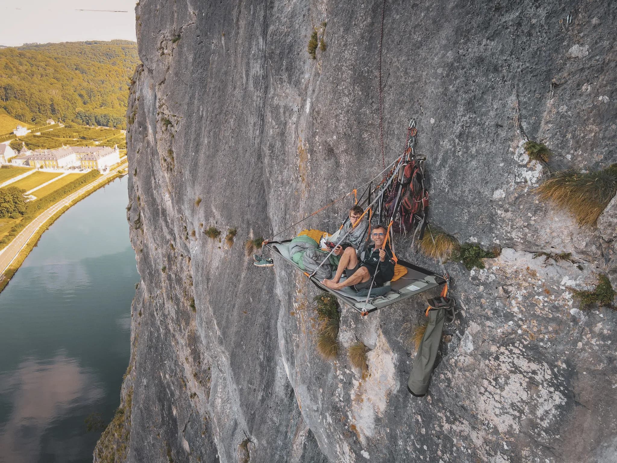 Deux grimpeurs détenteurs d'un portaledge, suspendu au-dessus d'une vallée verdoyante.