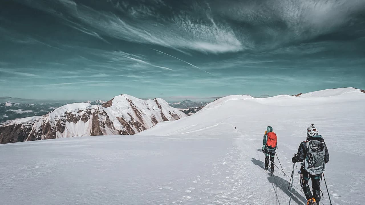 A snow-covered trail leading to majestic peaks, mountaineers exploring beneath a blue sky.