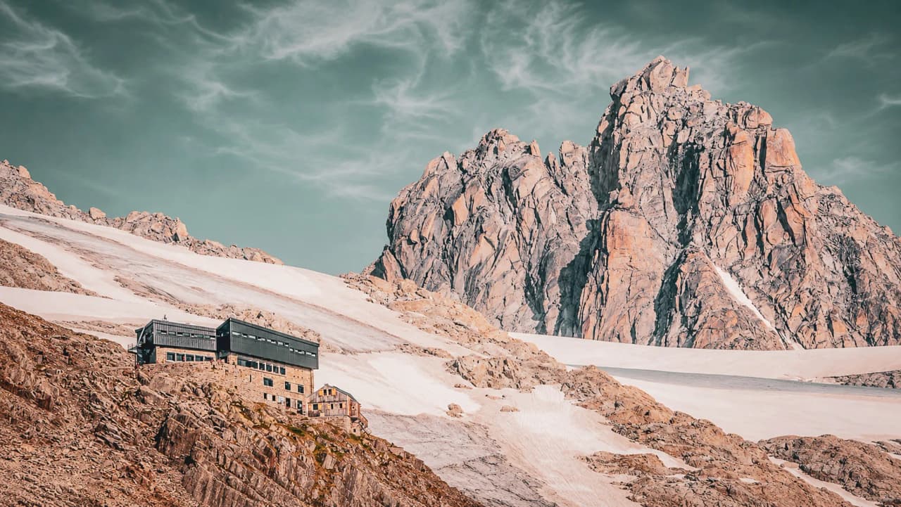 Mountain hut at the foot of majestic rocky cliffs, surrounded by glistening glaciers.