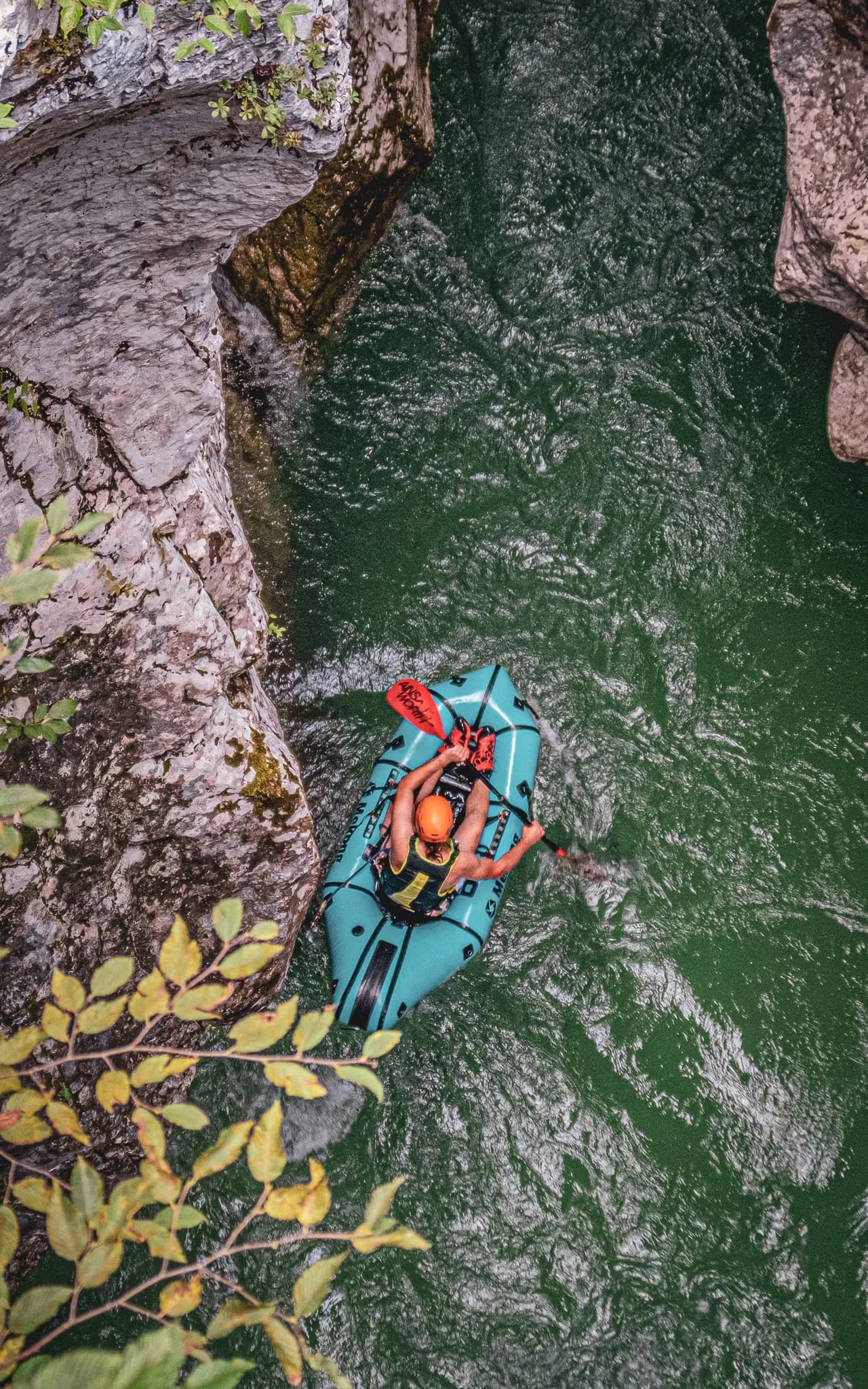 An adventurer paddling in a turquoise packraft, nestled between rocks on an alpine river.