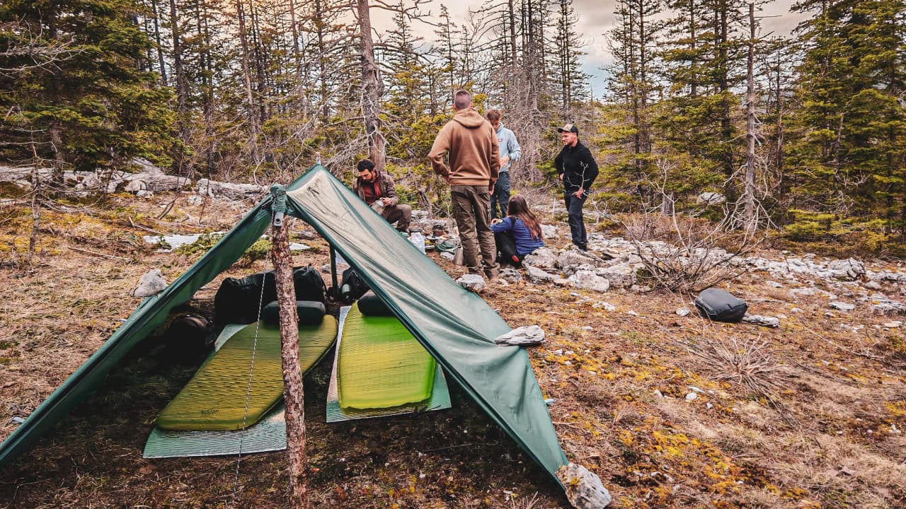 Groupe en pleine nature, sous un abri improvisé, apprenant la survie dans les forêts du Vercors.