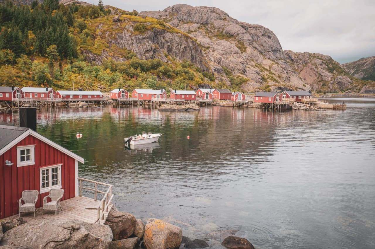 A landscape punctuated by red huts on the water's edge, surrounded by green mountains.
