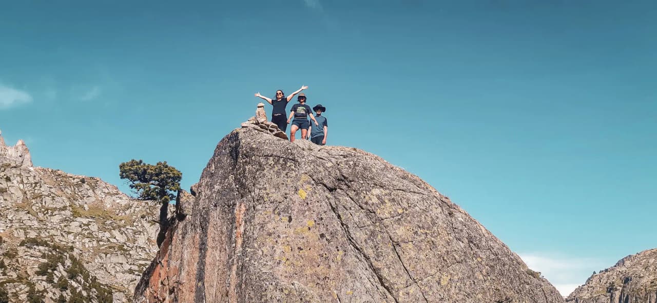 A group of happy hikers on top of a rock, under a brilliant blue sky.