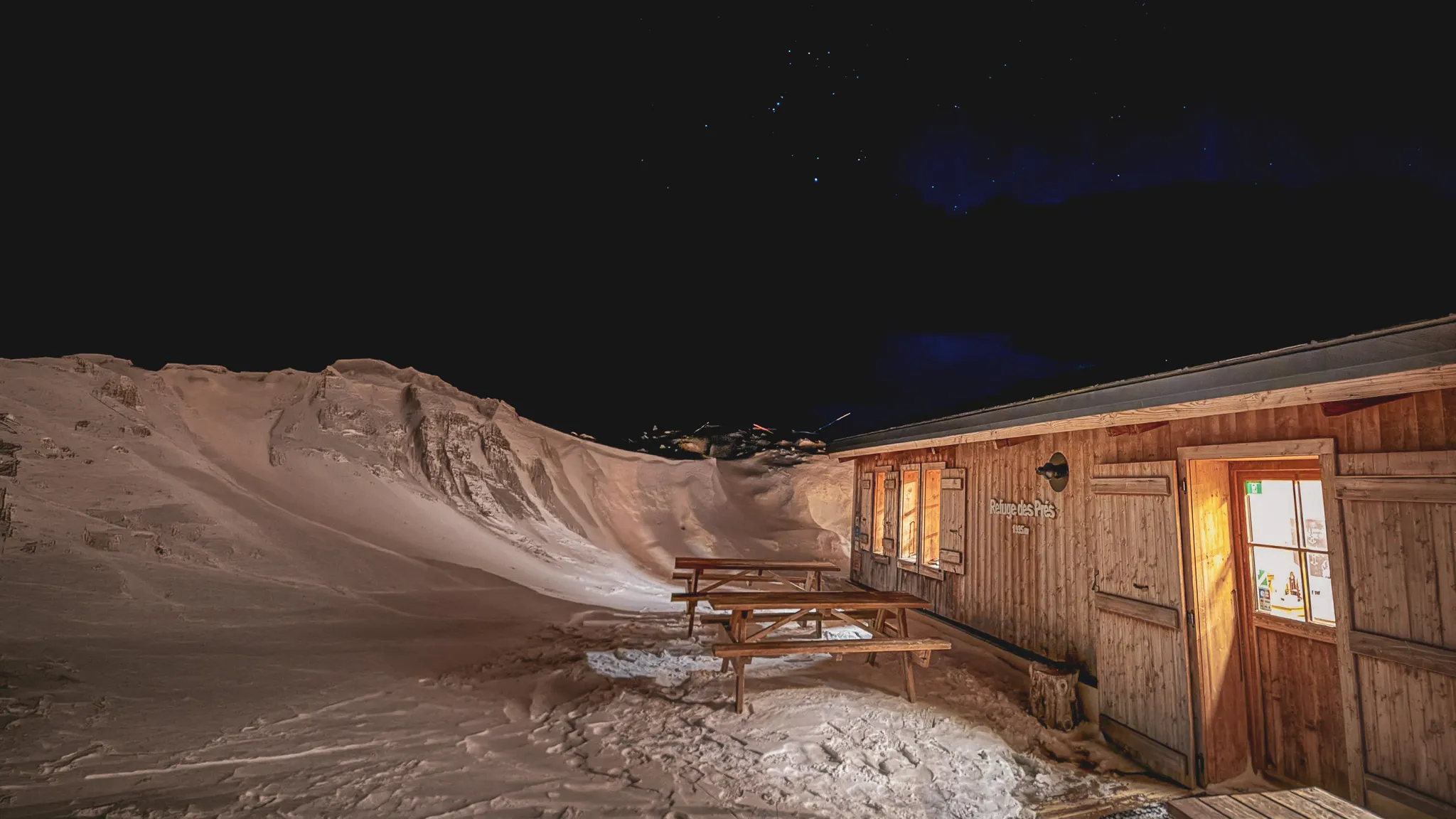 An illuminated wooden Mountain hut, surrounded by snow, under a starry sky. Escape to Mont Blanc.