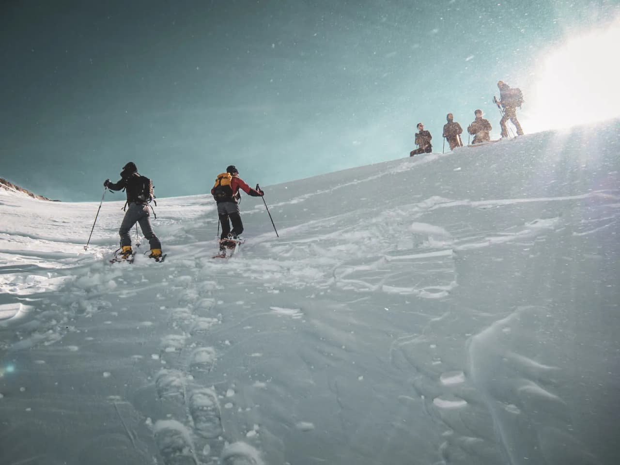 Deux randonneurs en raquettes gravissent une neige immaculée sous un ciel bleu, entourés de montagne.