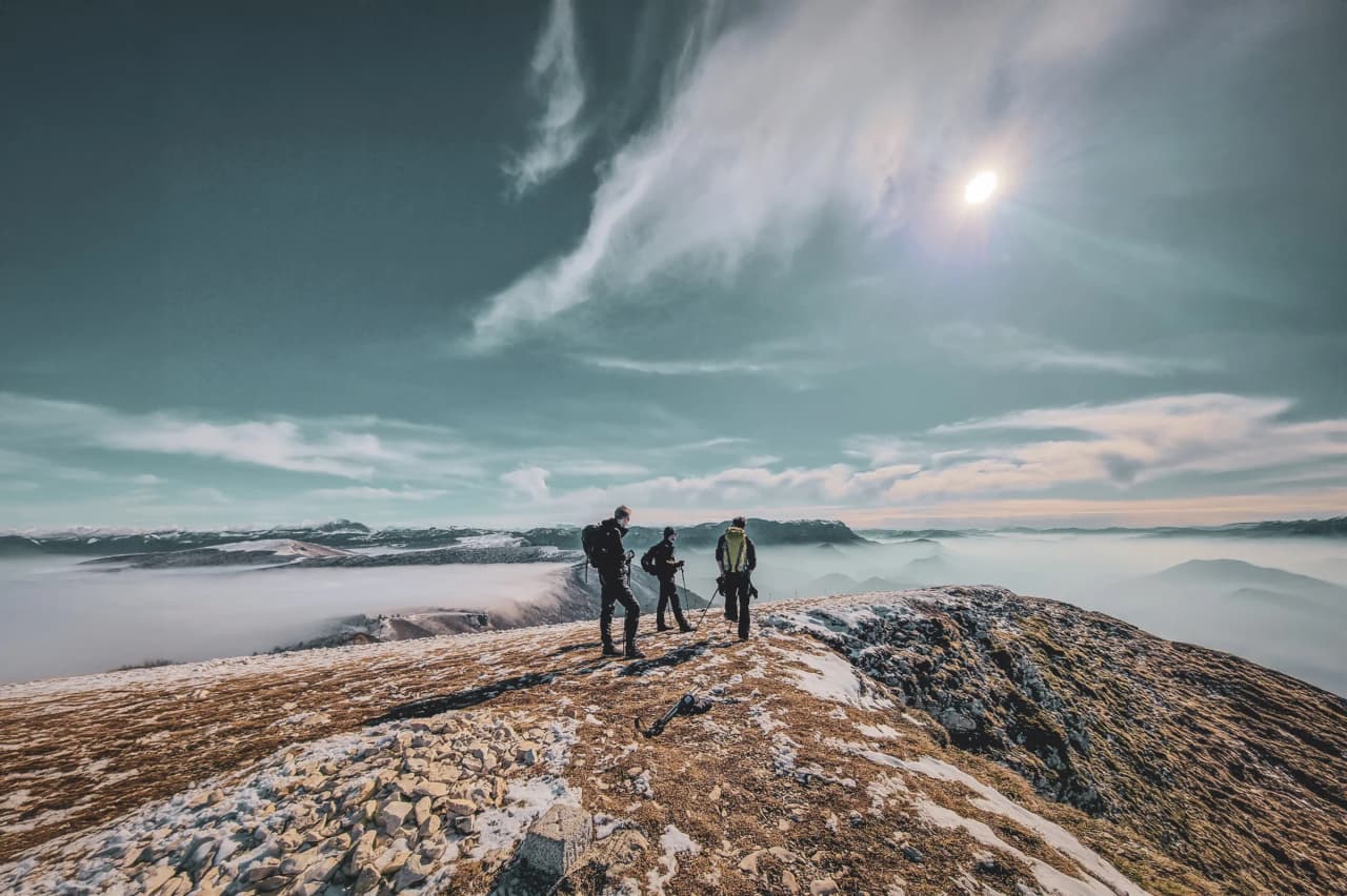 Trois randonneurs sur un sommet, entourés de paysages montagneux et d'une mer de nuages.