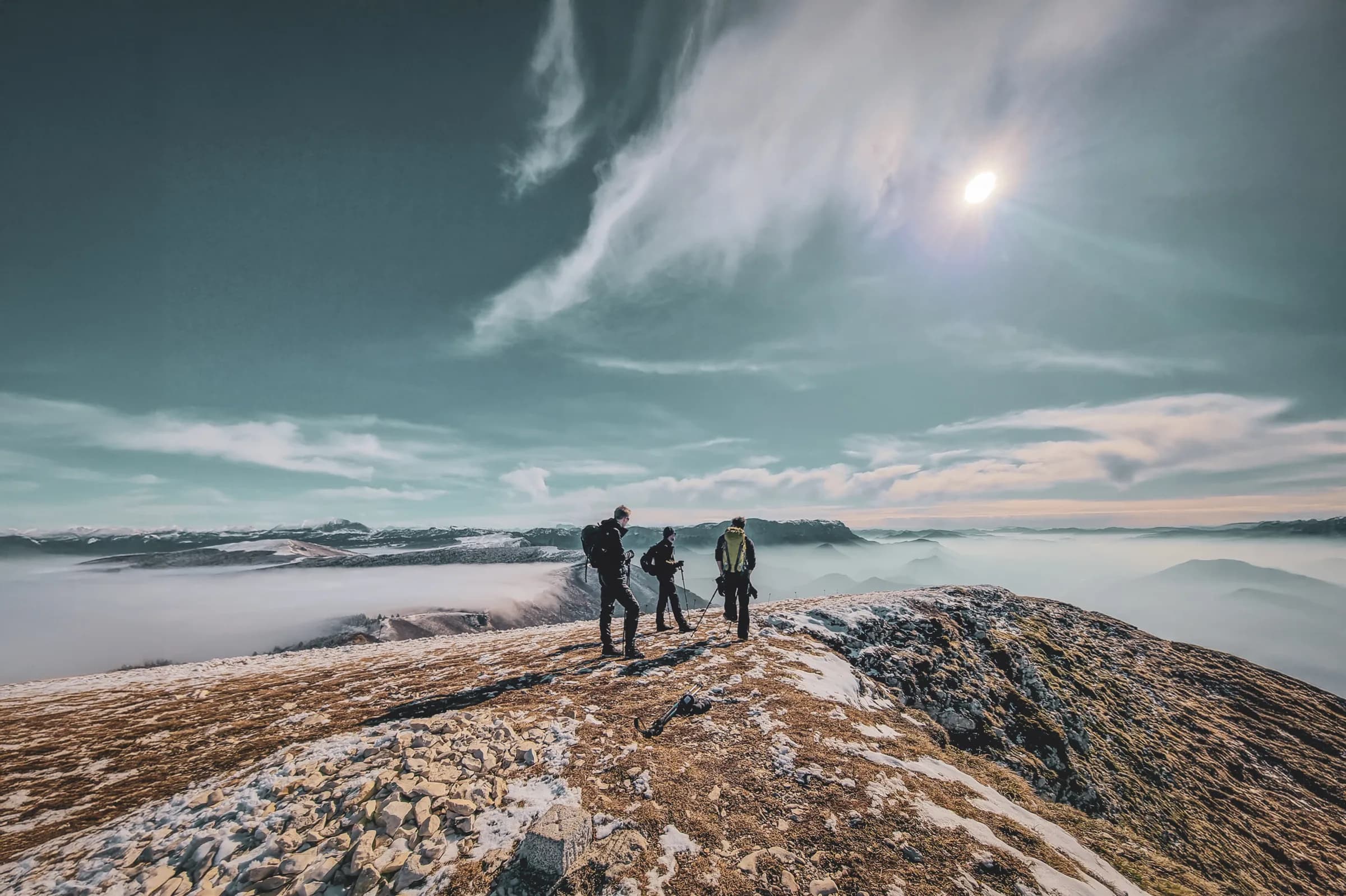 Three hikers on a summit, surrounded by mountain scenery and a sea of clouds.