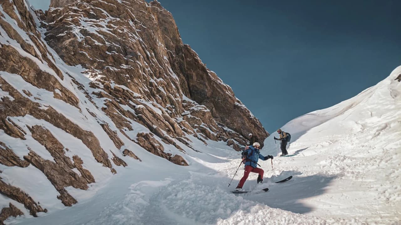 Skieurs évoluant sur une pente neigeuse, entourés de paysages montagneux spectaculaires.