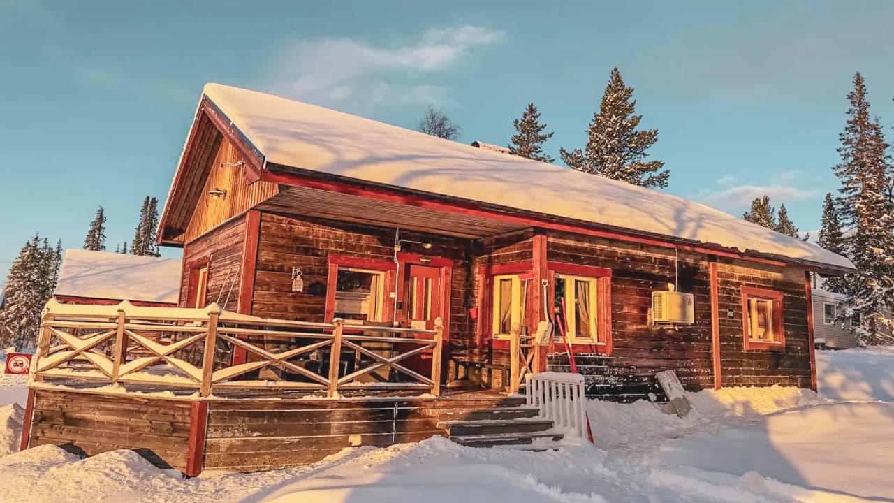 A cosy wooden chalet surrounded by snow, under a blue sky in Swedish Lapland.