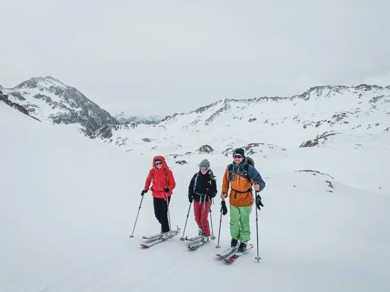 Drie skiërs trekken door een besneeuwd landschap op de Mont Thabor, onder een bewolkte hemel.