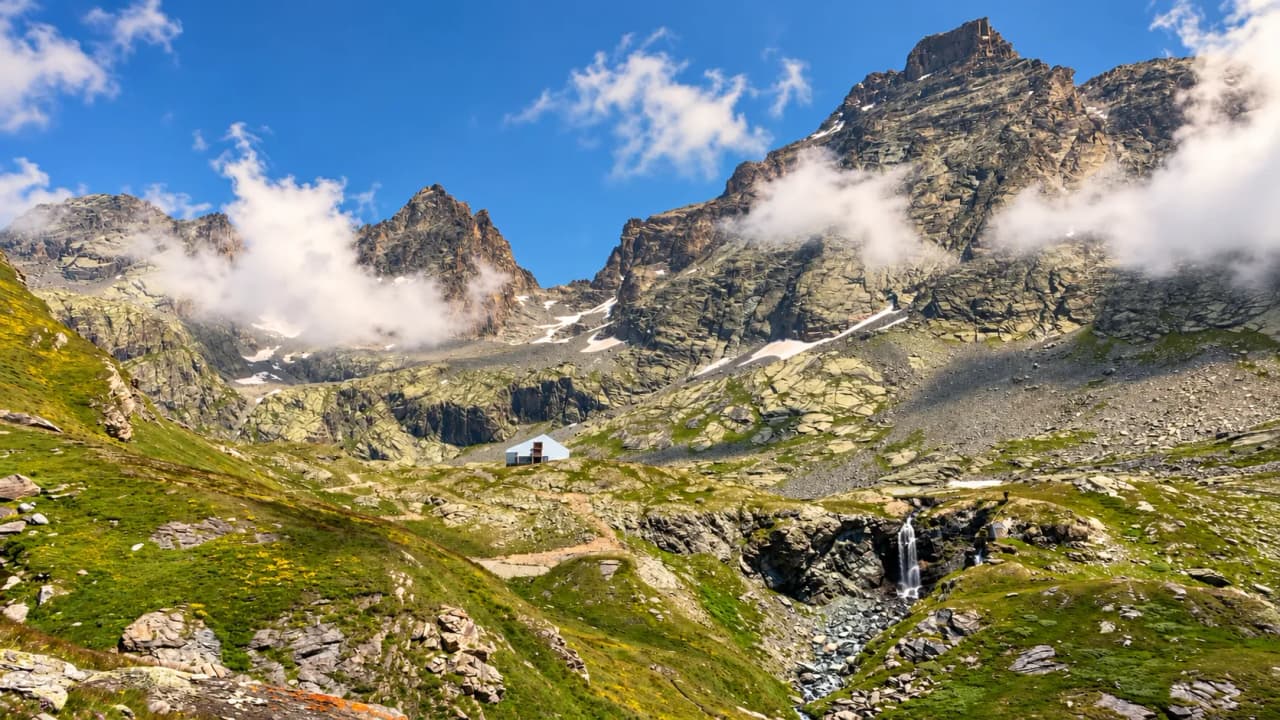 A wonderful alpine view featuring majestic mountains, a secluded mountain hut and sparkling waterfalls.