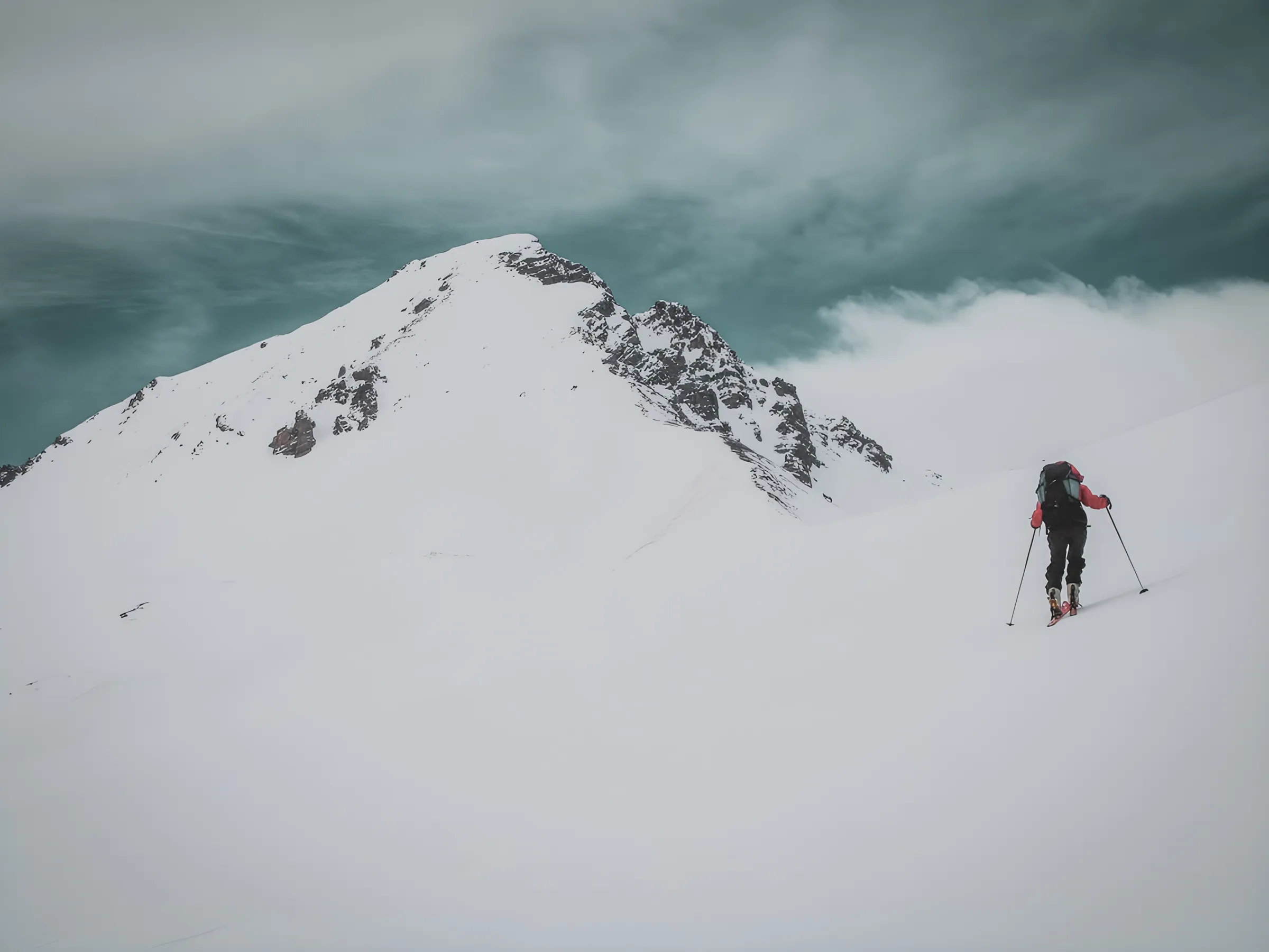 A lone skier climbs a snowy mountain under a dramatic sky, inviting adventure.