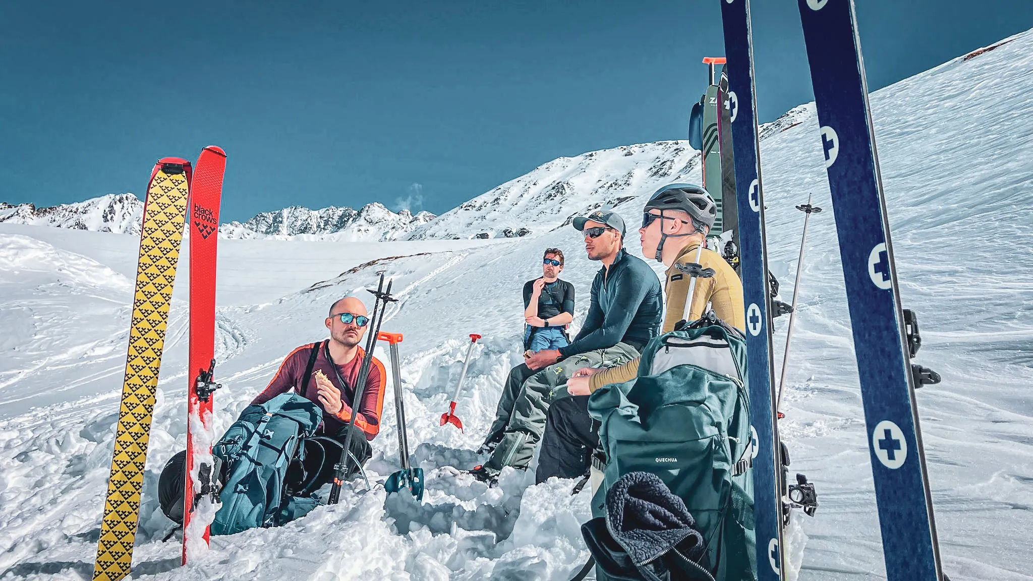 Groupe d'aventuriers en pause, skis plantés dans la neige, sous un ciel bleu éclatant.