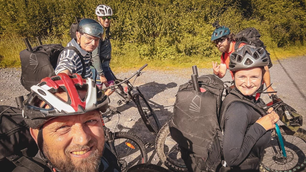 Five smiling adventurers on mountain bikes, ready for a wilderness expedition.