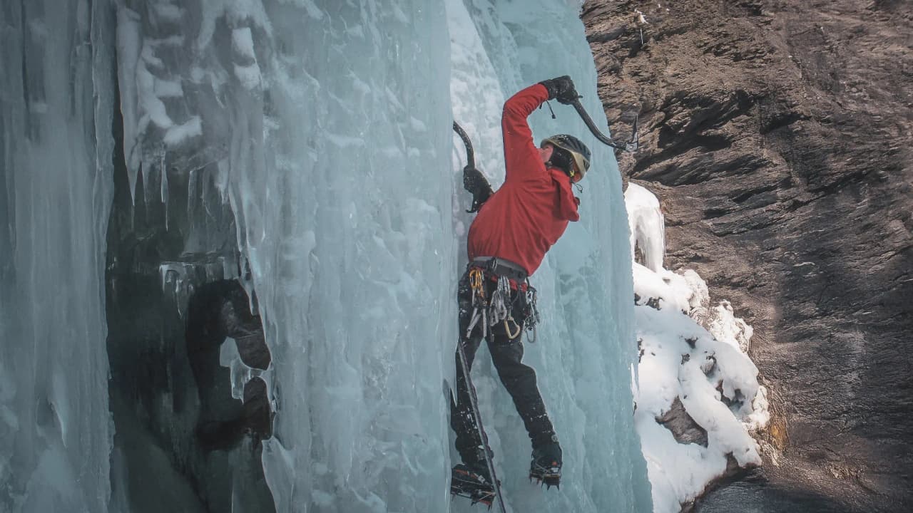 A mountaineer climbs a glistening ice wall in the majestic landscape of the Alps.