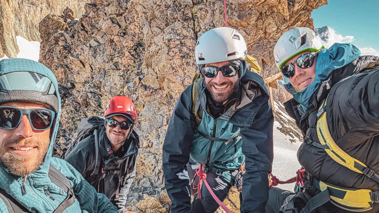 Quatre alpinistes souriants posent ensemble sur une paroi rocheuse, prêts pour l'aventure.